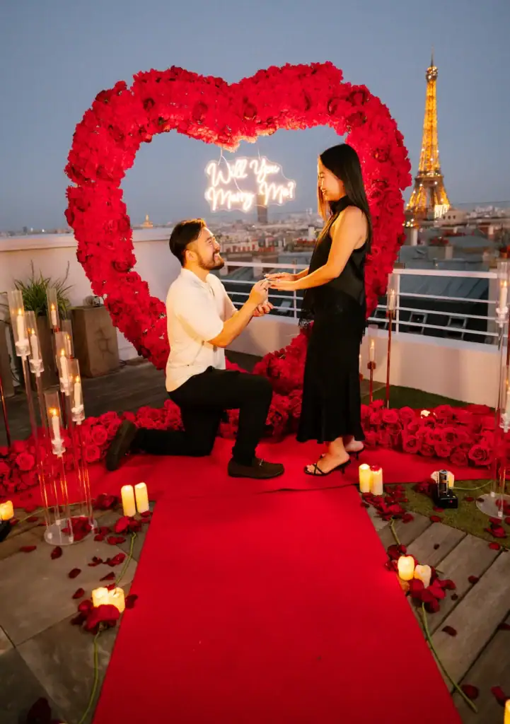 Romantic proposal on a Paris rooftop with Eiffel Tower view and floral heart backdrop.